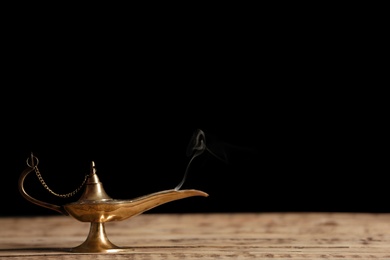 Aladdin lamp of wishes on wooden table against black background