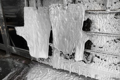 Photo of Auto mats covered with foam hanging at car wash, closeup