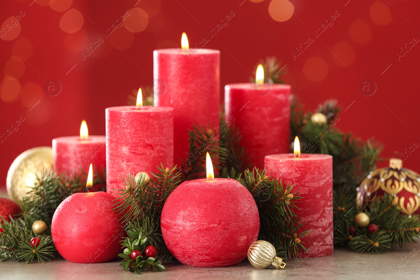 Photo of Burning candles and Christmas decor on table against red background with bokeh effect