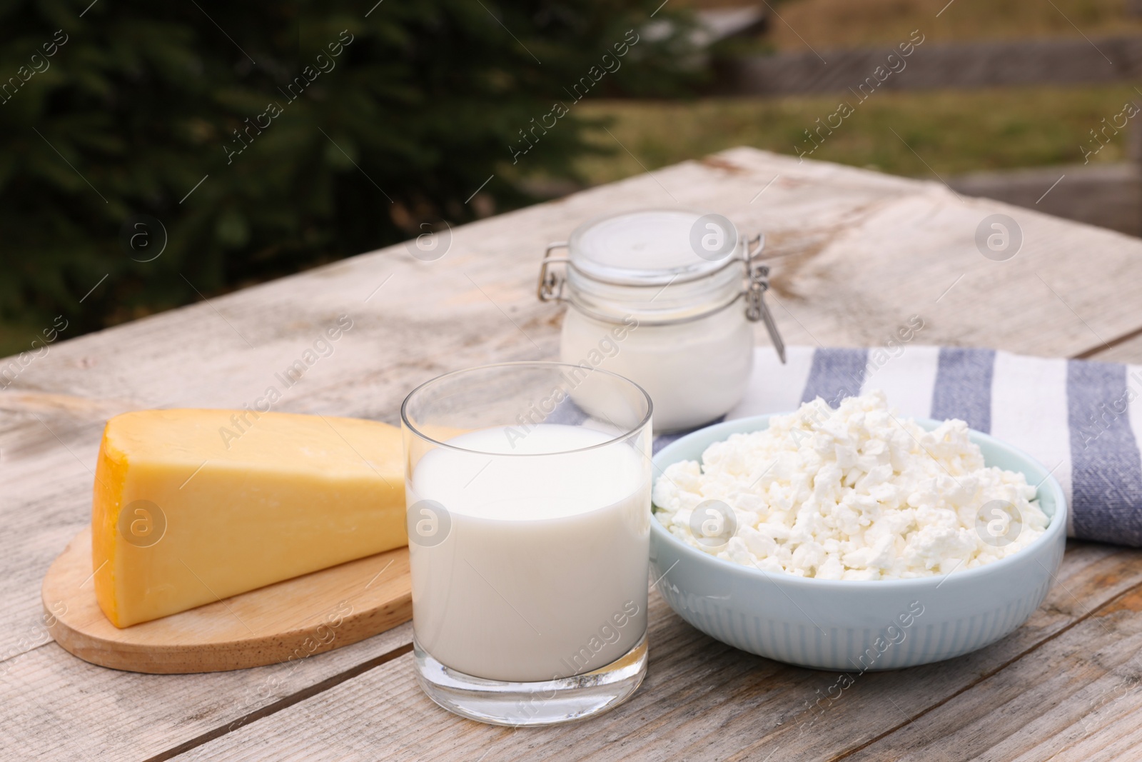 Photo of Tasty cottage cheese and other fresh dairy products on wooden table outdoors