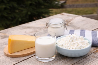 Tasty cottage cheese and other fresh dairy products on wooden table outdoors