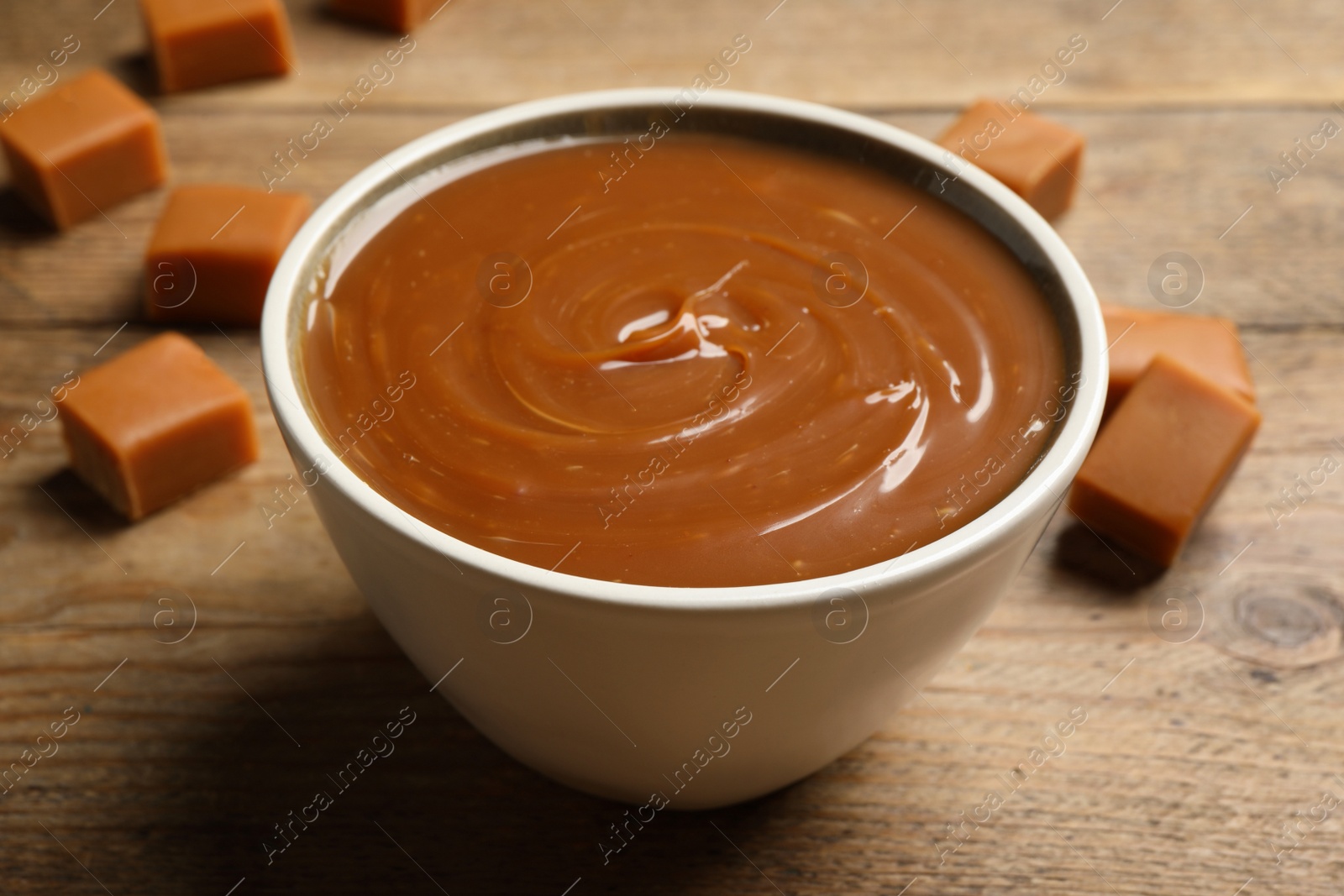 Photo of Yummy salted caramel in bowl and candies on wooden table, closeup