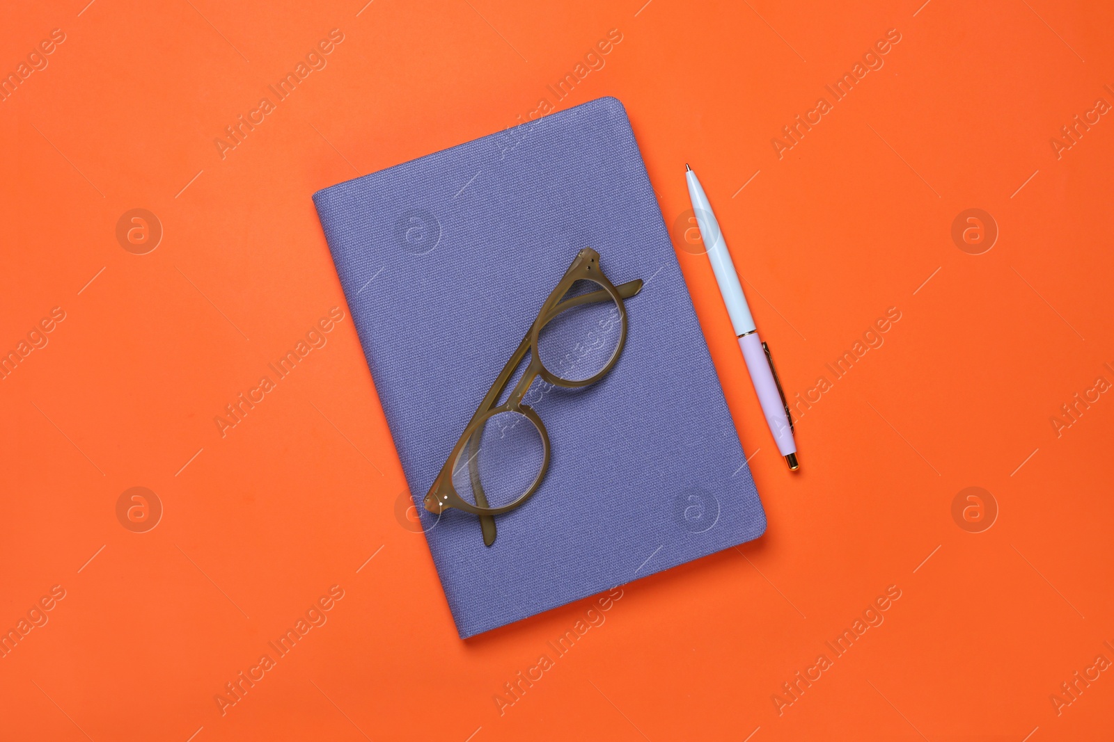 Photo of Closed blue notebook, eyeglasses and pen on orange background, flat lay