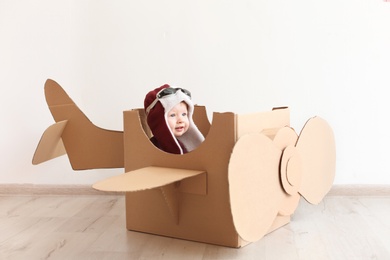 Adorable little child playing with cardboard plane indoors