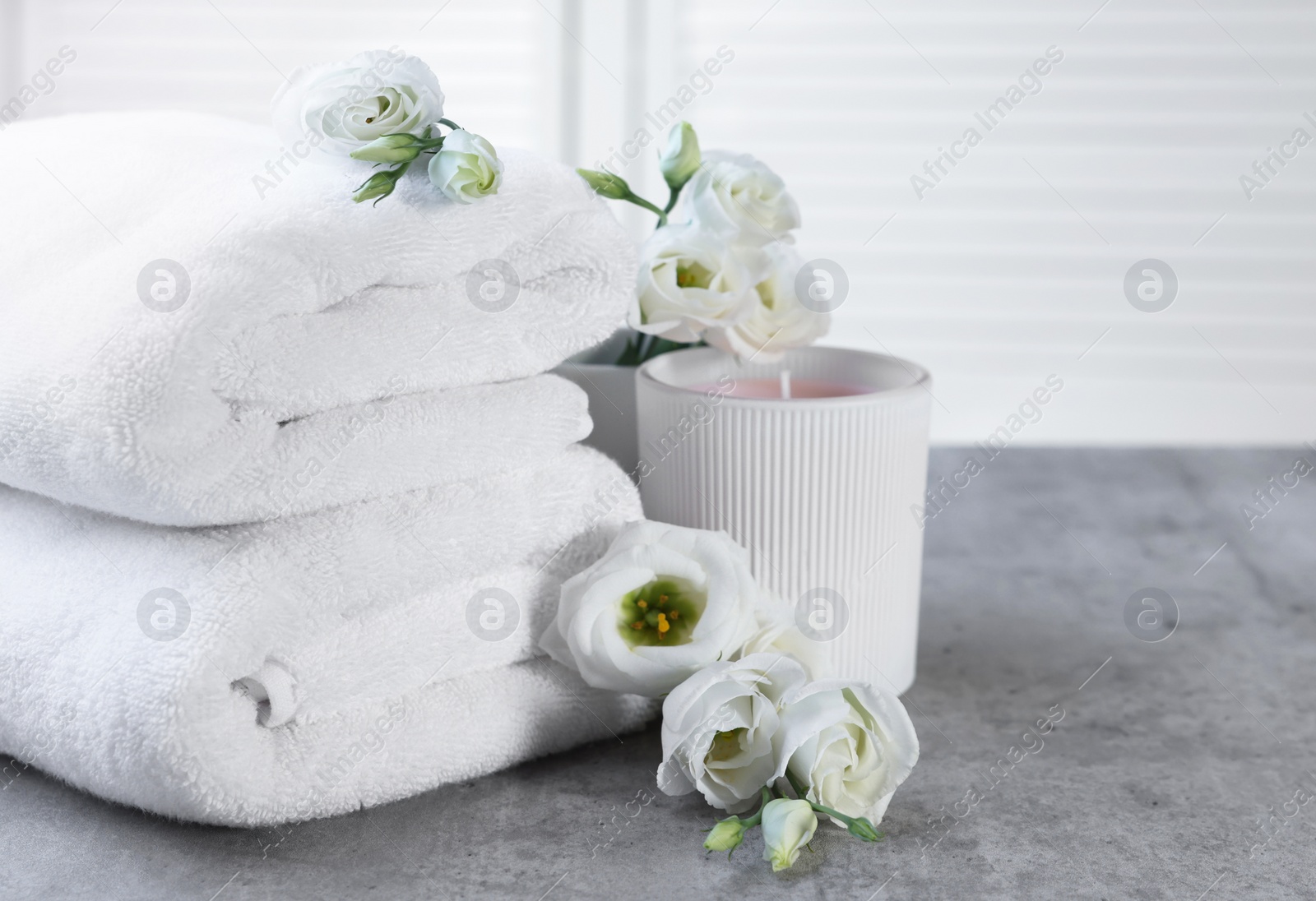 Photo of Scented candle, folded towels and eustoma flowers on gray marble table, space for text