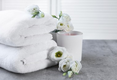 Photo of Scented candle, folded towels and eustoma flowers on gray marble table, space for text