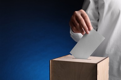 Photo of Woman putting her vote into ballot box on dark blue background, closeup. Space for text