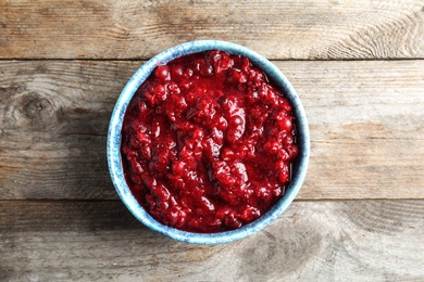 Photo of Bowl of tasty cranberry sauce on wooden background, top view