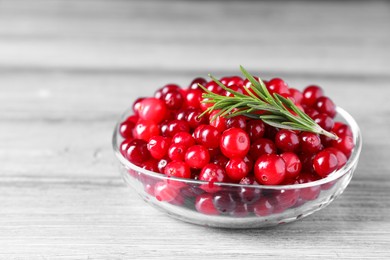 Photo of Fresh ripe cranberries and rosemary in bowl on grey wooden table, closeup