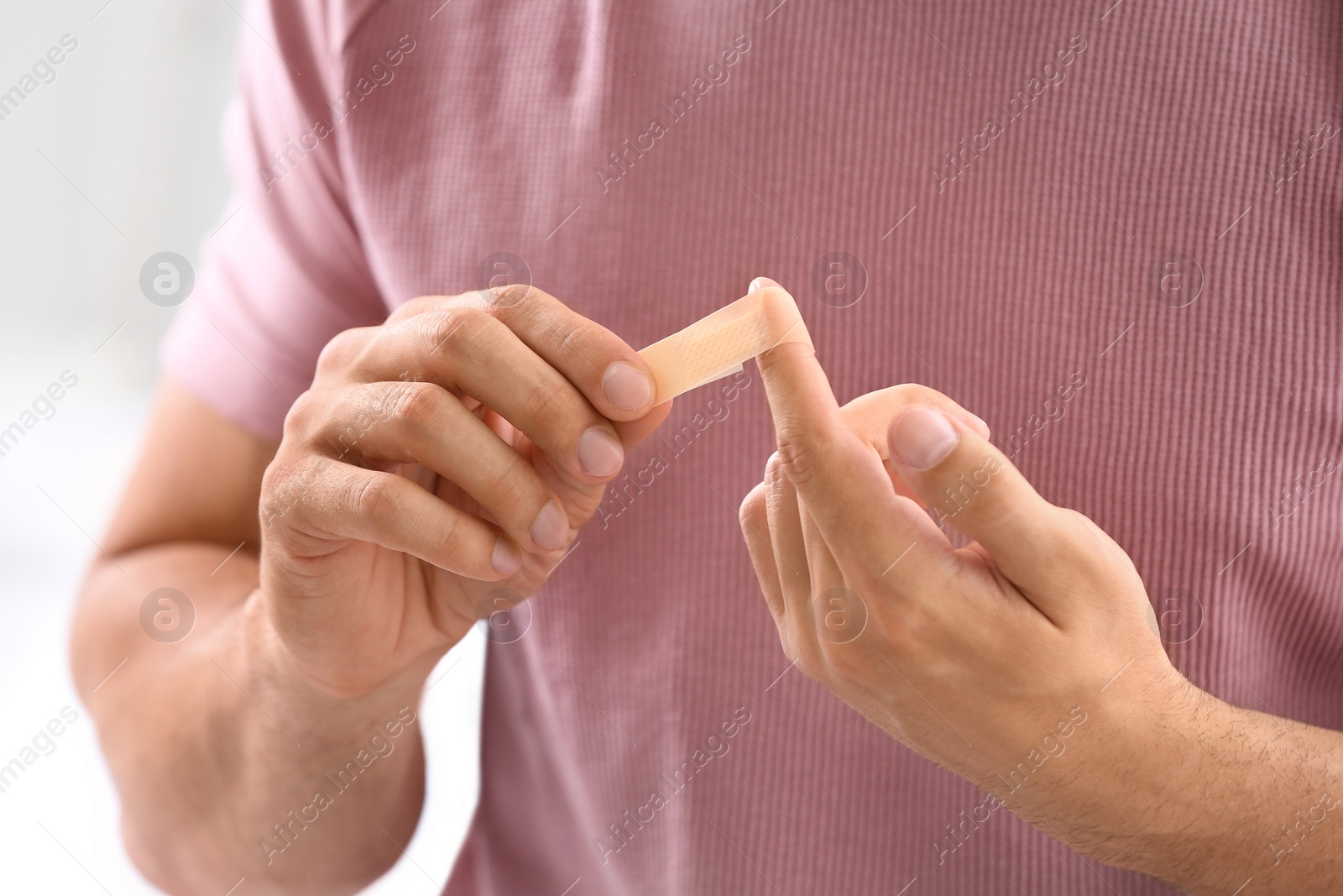 Photo of Man applying adhesive bandage on finger, closeup view