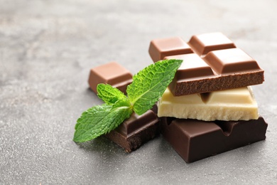 Photo of Different kinds of chocolate with mint on gray table