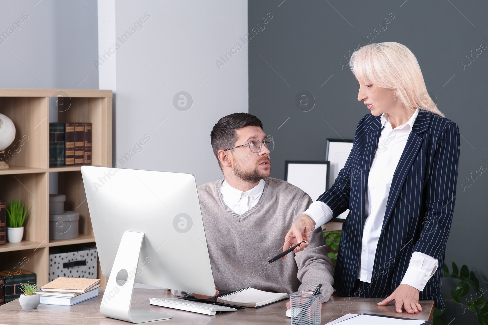 Photo of Boss discussing work issues with employee and pointing at notebook in office