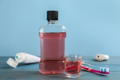 Photo of Bottle and glass with mouthwash near other oral hygiene products on light blue wooden table