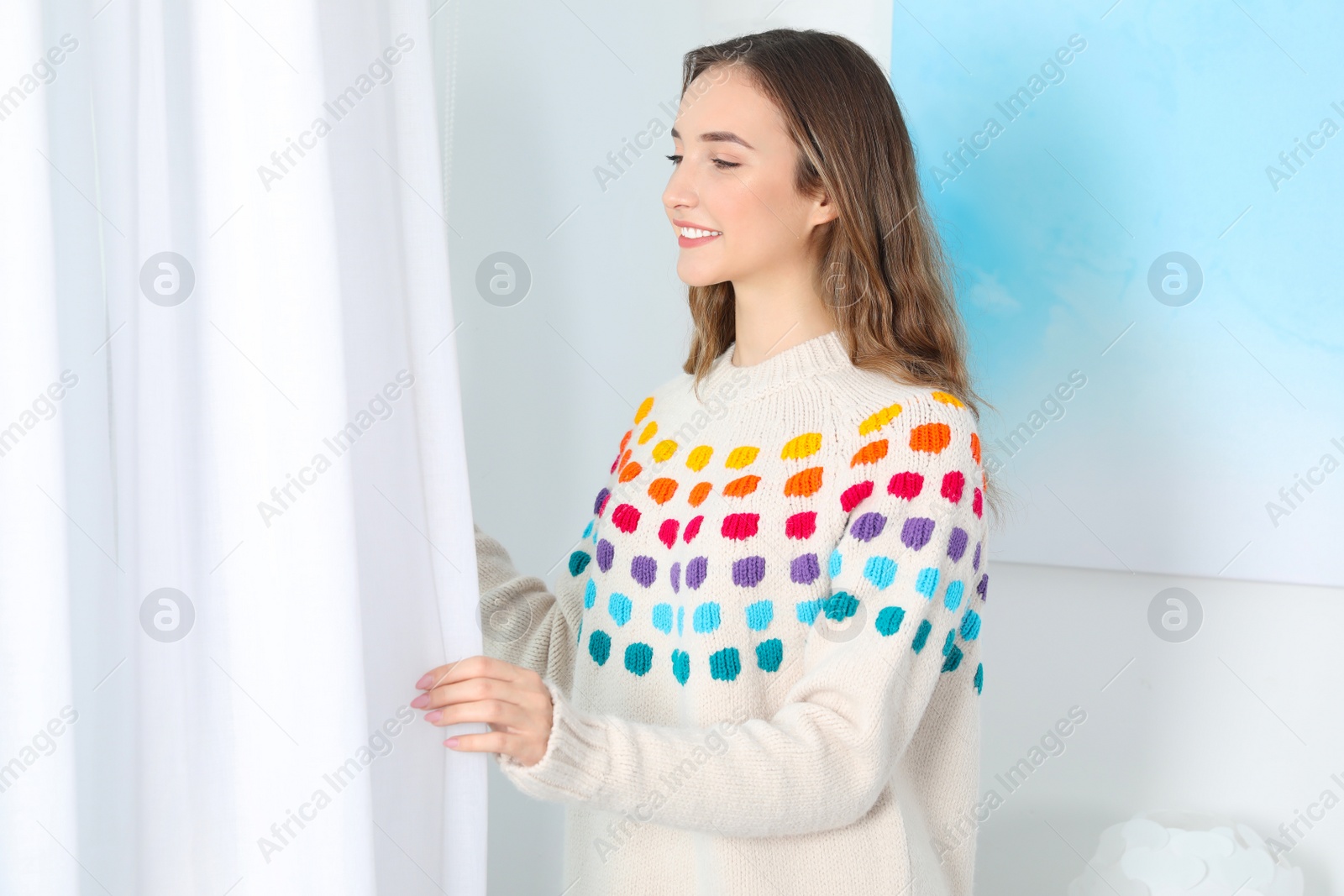 Photo of Beautiful teenage girl in warm cozy sweater looking out window at home