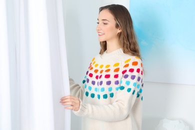 Photo of Beautiful teenage girl in warm cozy sweater looking out window at home