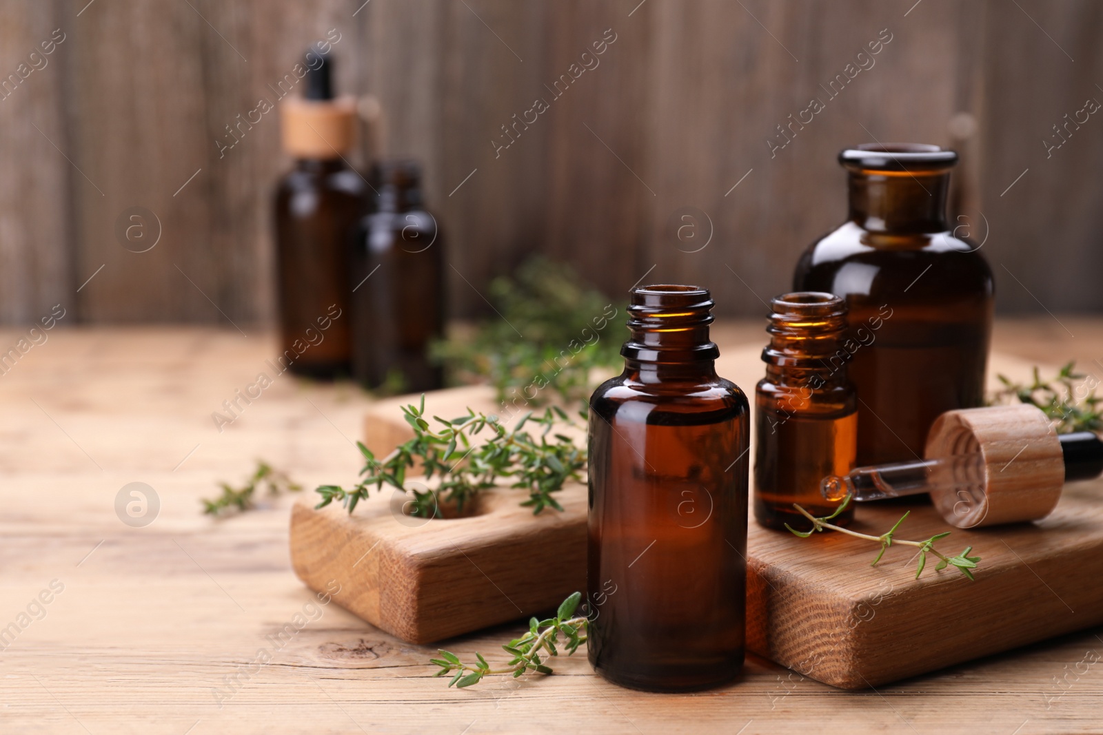 Photo of Thyme essential oil and fresh plant on wooden table, space for text