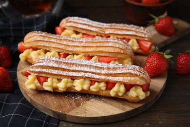 Photo of Delicious eclairs filled with cream and strawberries on wooden table