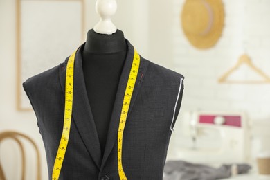 Photo of Mannequin with unfinished jacket and measuring tape in tailor shop, space for text