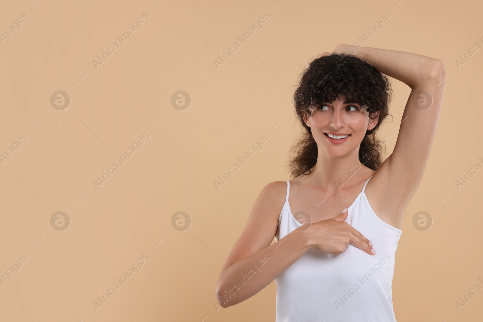 Photo of Smiling young woman doing breast self-examination on light brown background. Space for text