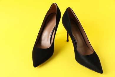Pair of elegant black high heel shoes on yellow background