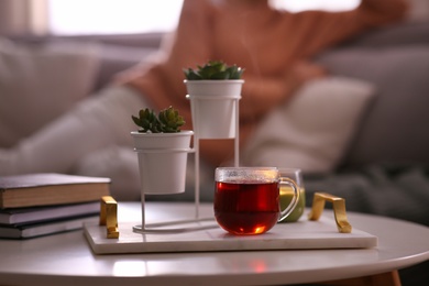 Photo of Woman relaxing at home, focus on tray with cup of tea and succulent plants. Cozy atmosphere