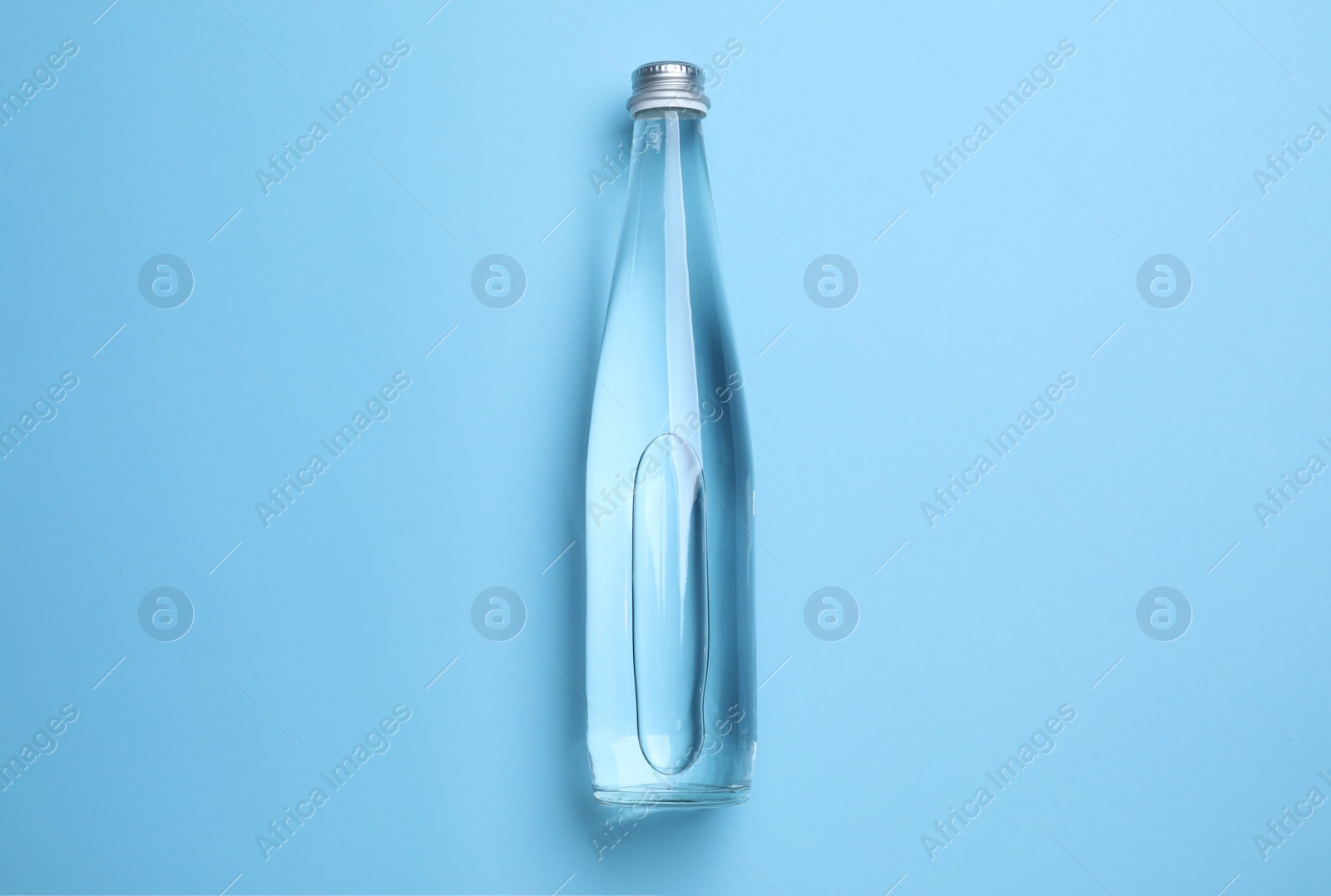 Photo of Glass bottle with water on light blue background, top view