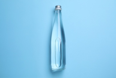 Glass bottle with water on light blue background, top view