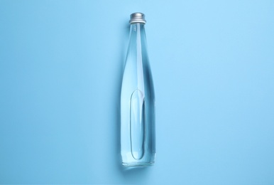 Photo of Glass bottle with water on light blue background, top view