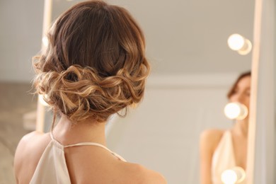 Woman with beautiful hairstyle near mirror in salon