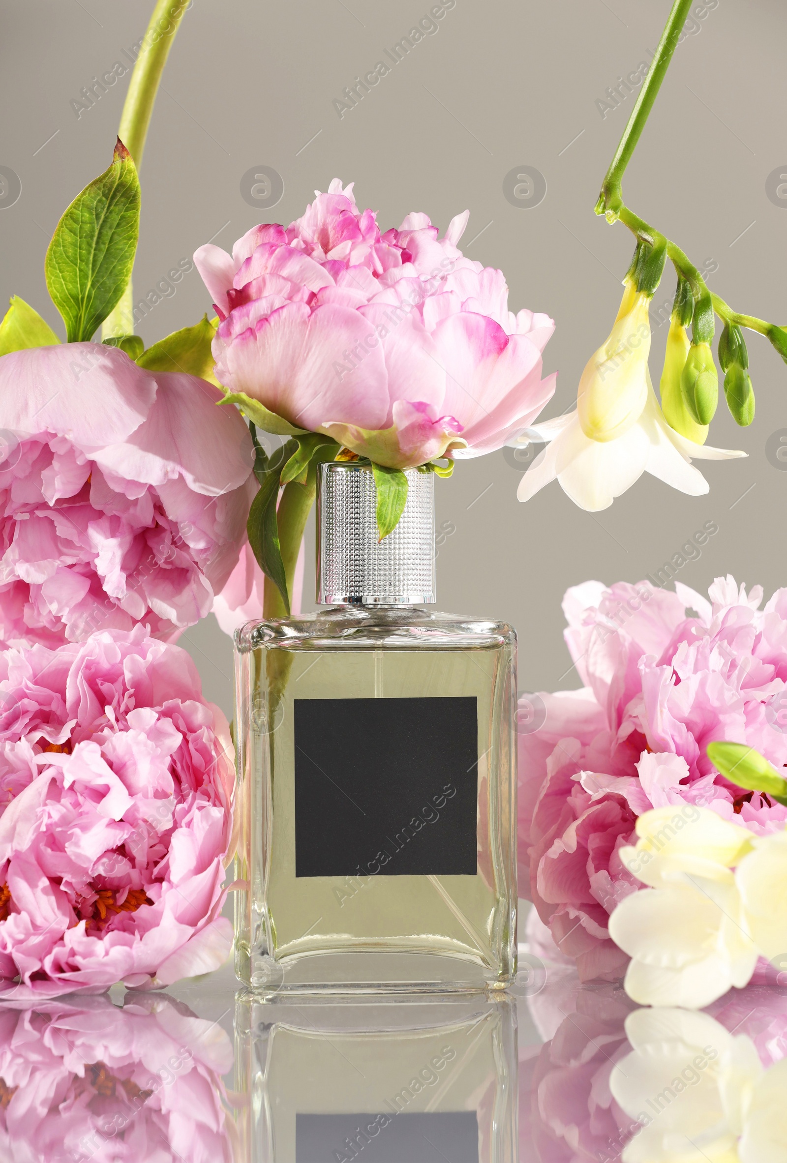 Photo of Bottle of luxury perfume and floral decor on mirror surface against light grey background