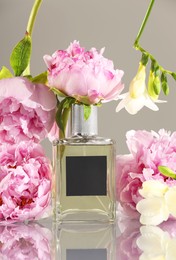 Photo of Bottle of luxury perfume and floral decor on mirror surface against light grey background
