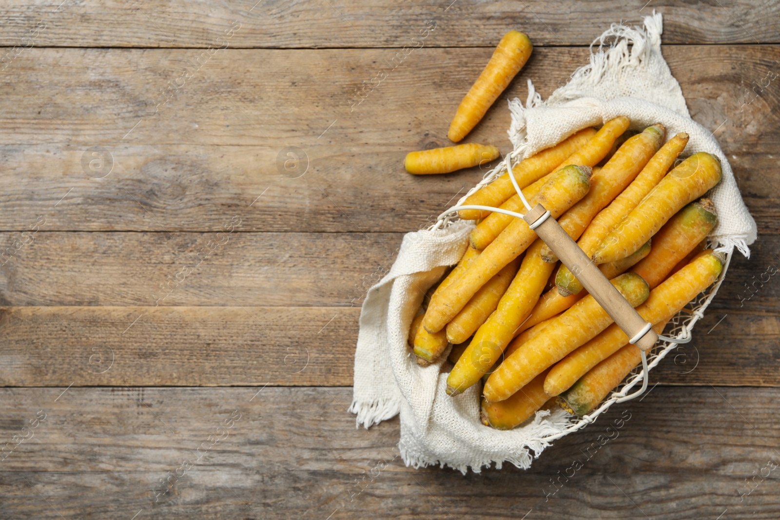 Photo of Raw yellow carrots in metal basket on wooden table, top view. Space for text