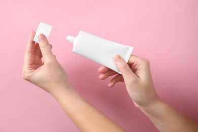 Photo of Woman opening tube of hand cream on pink background, closeup