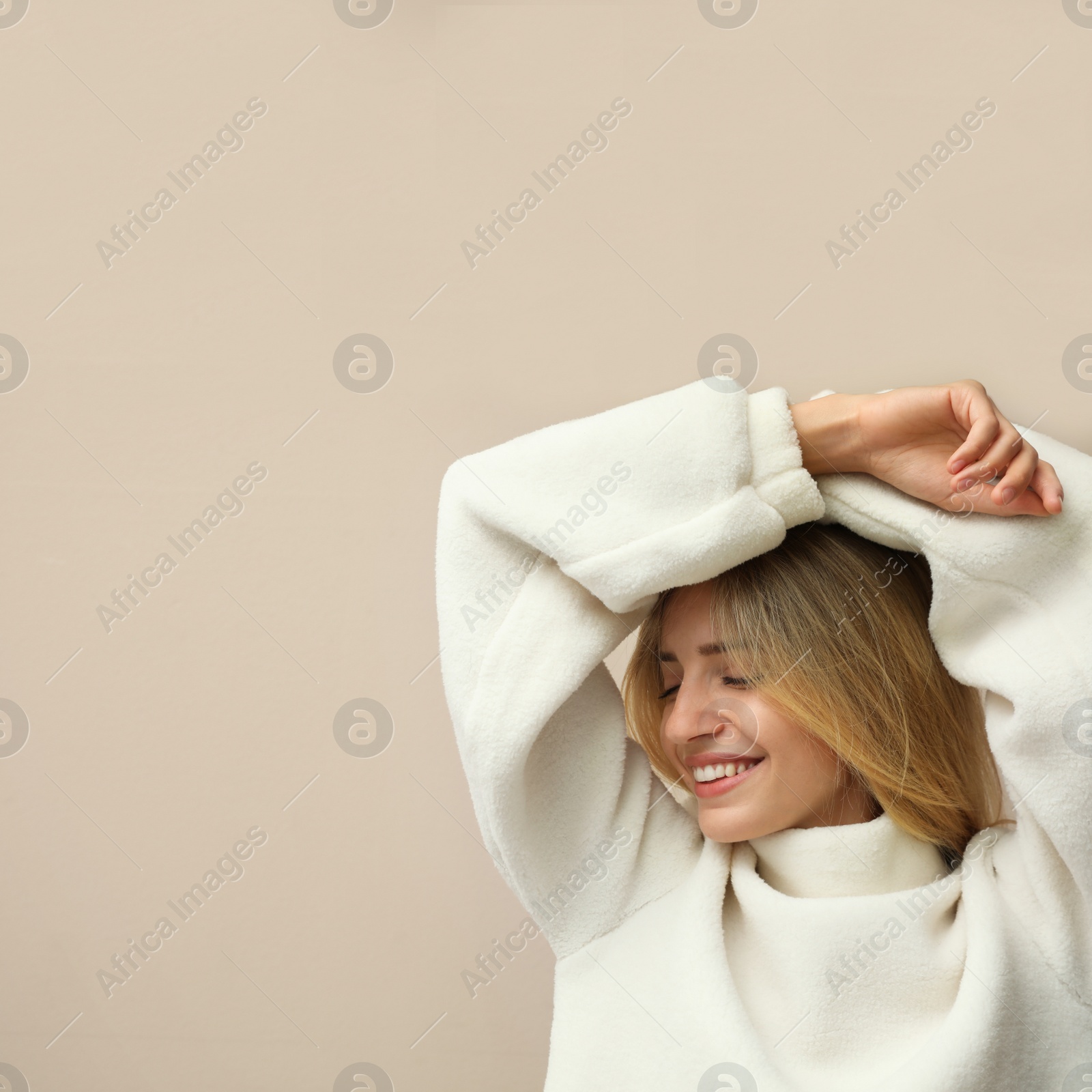 Photo of Beautiful young woman wearing knitted sweater on beige background. Space for text
