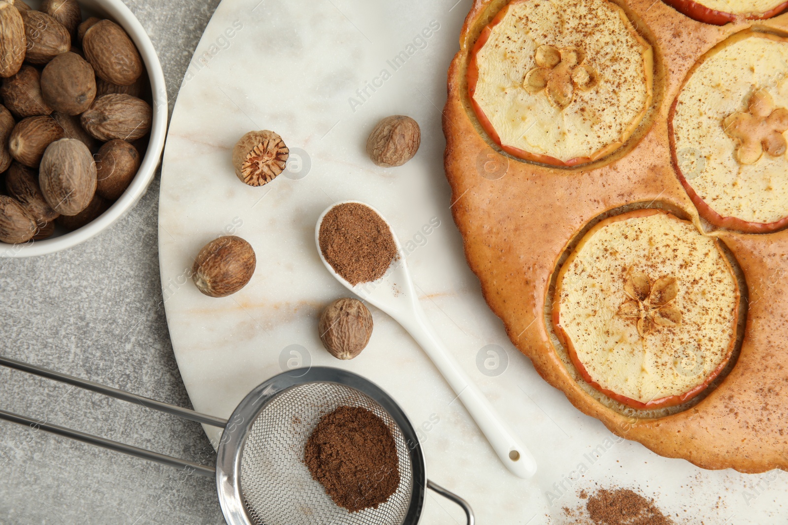 Photo of Nutmeg powder, seeds and tasty apple pie on light grey table, flat lay