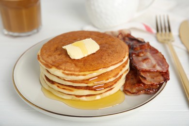 Delicious pancakes with maple syrup, butter and fried bacon on white wooden table, closeup