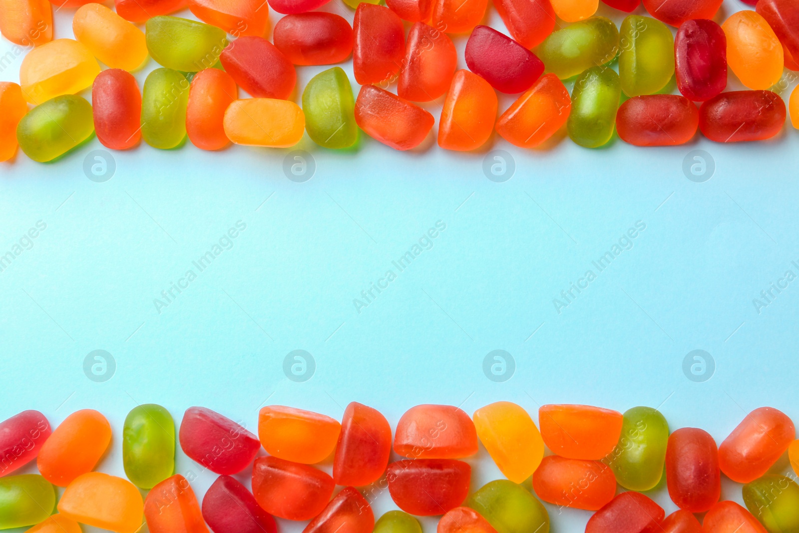 Photo of Frame of sweet jelly candies on blue background, top view. Space for text