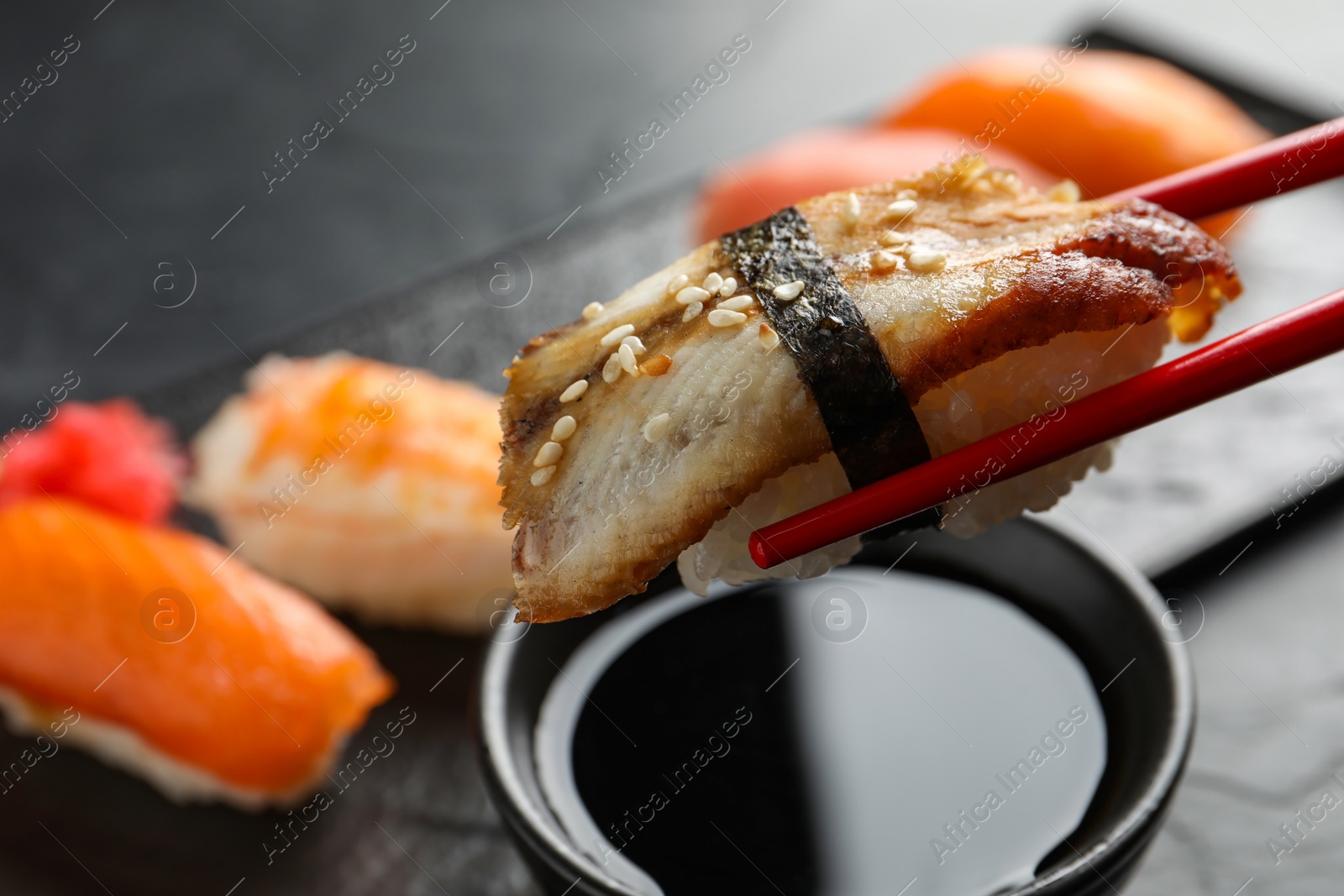 Photo of Dipping delicious nigiri sushi into soy sauce on black table, closeup