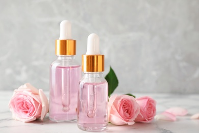 Bottles of essential oil and roses on marble table