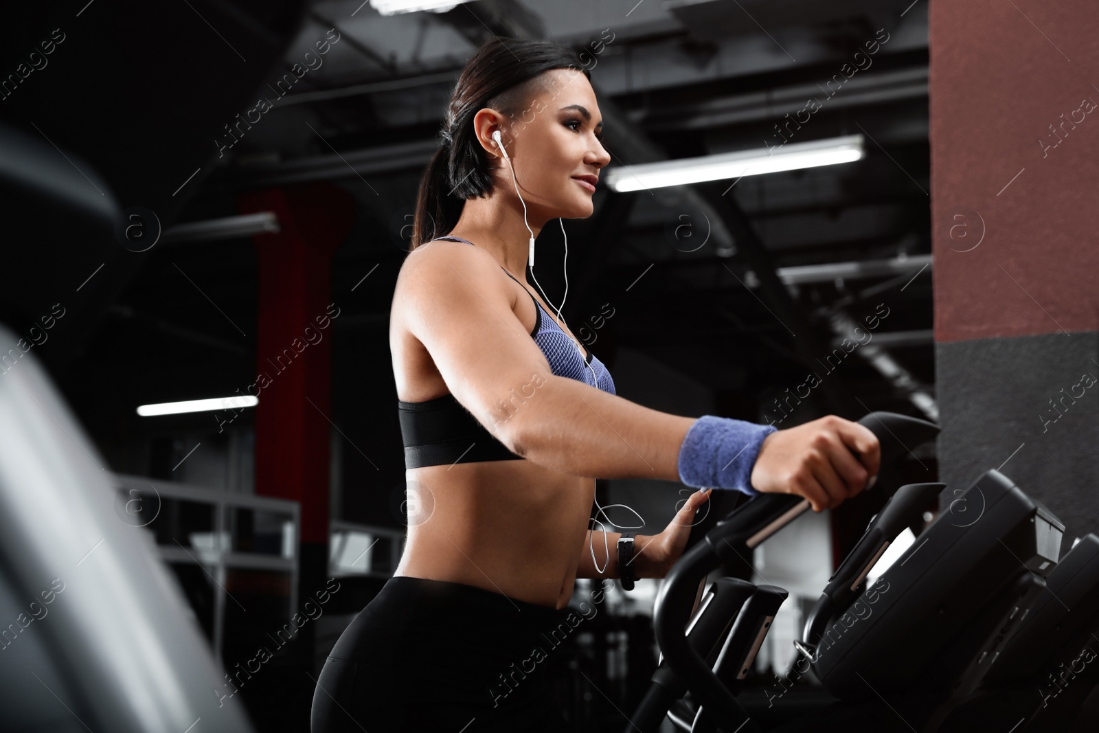 Photo of Young woman working out on elliptical trainer in modern gym