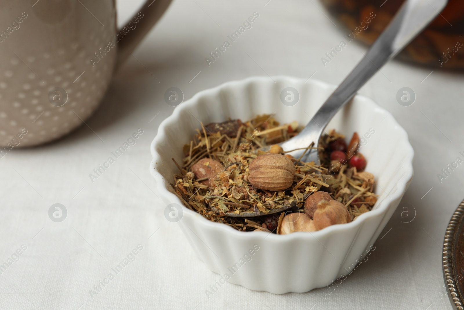 Photo of Aromatic dried herbs and berries for tea in bowl on white fabric, closeup