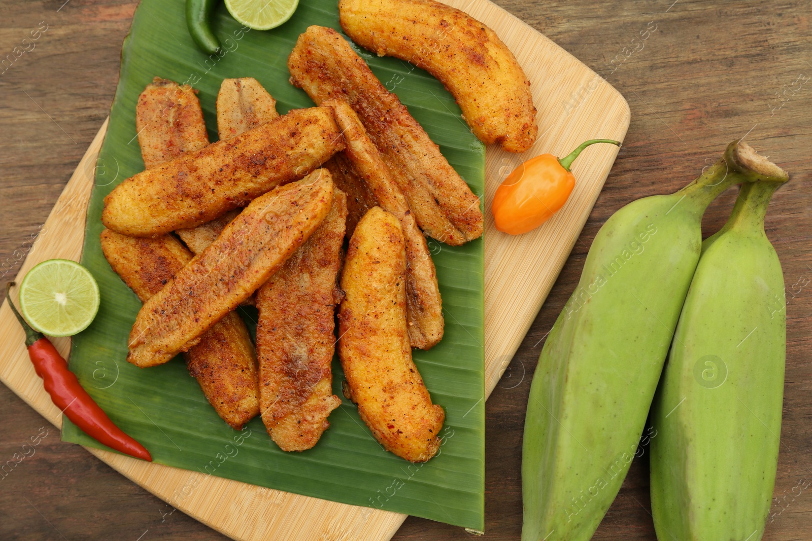 Photo of Delicious fried bananas, different peppers and cut limes on wooden table, flat lay