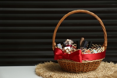 Photo of Wicker gift basket with cosmetic products on white table against dark background. Space for text