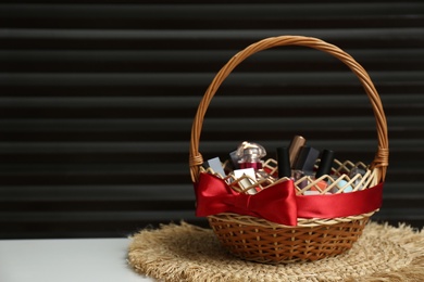 Wicker gift basket with cosmetic products on white table against dark background. Space for text