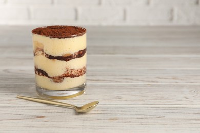 Photo of Delicious tiramisu in glass and spoon on light wooden table. Space for text