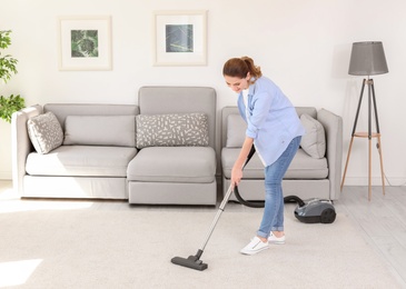 Photo of Woman removing dirt from carpet with vacuum cleaner at home