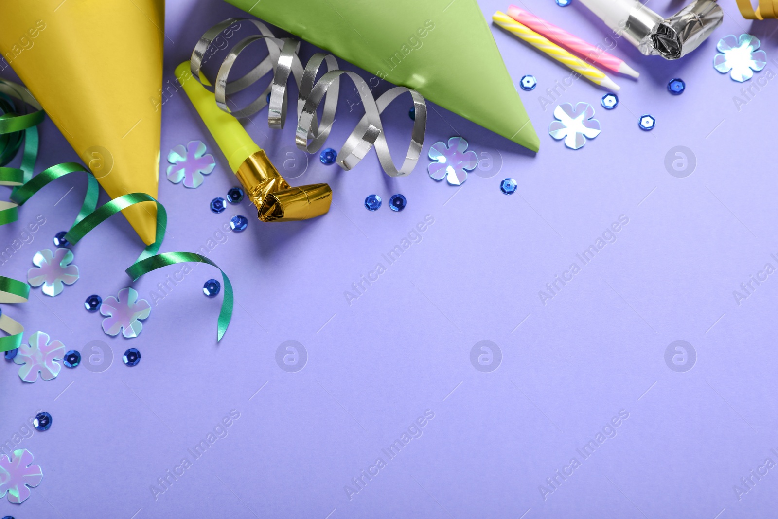 Photo of Birthday celebration. Party hats, blower, candles and decorative accessories on violet background, flat lay. Space for text