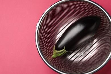 Photo of Colander with fresh eggplant on pink table, top view. Space for text