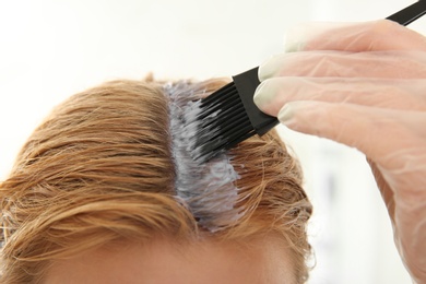 Photo of Young woman applying hair dye on roots against light background, closeup