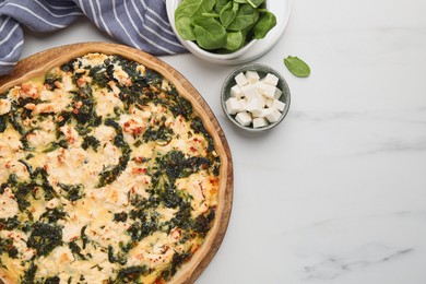 Delicious homemade spinach quiche and ingredients on white marble table, flat lay. Space for text